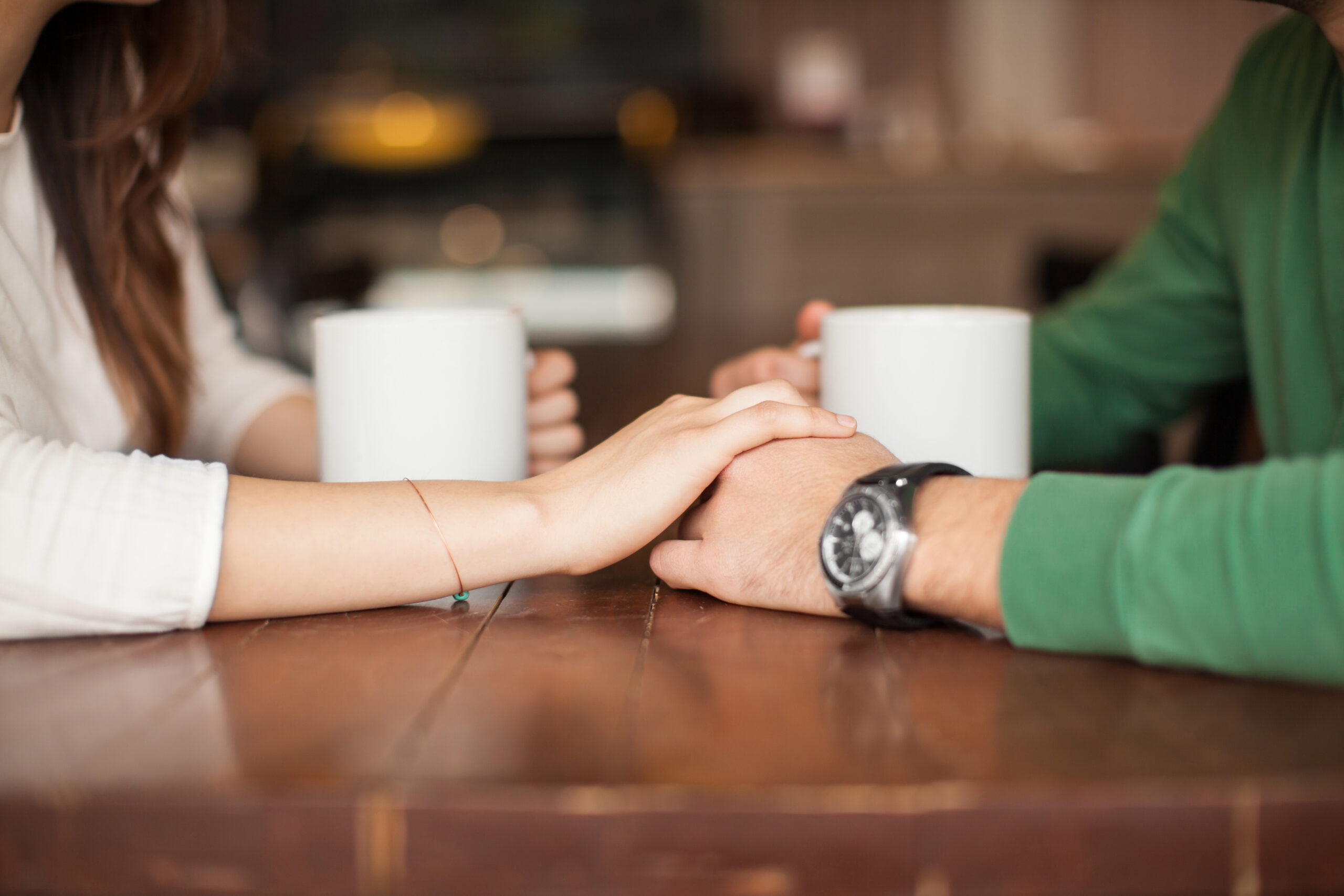 Closeup of the hands of a young woman holding the hands of her boyfriend while having coffee at a cafe